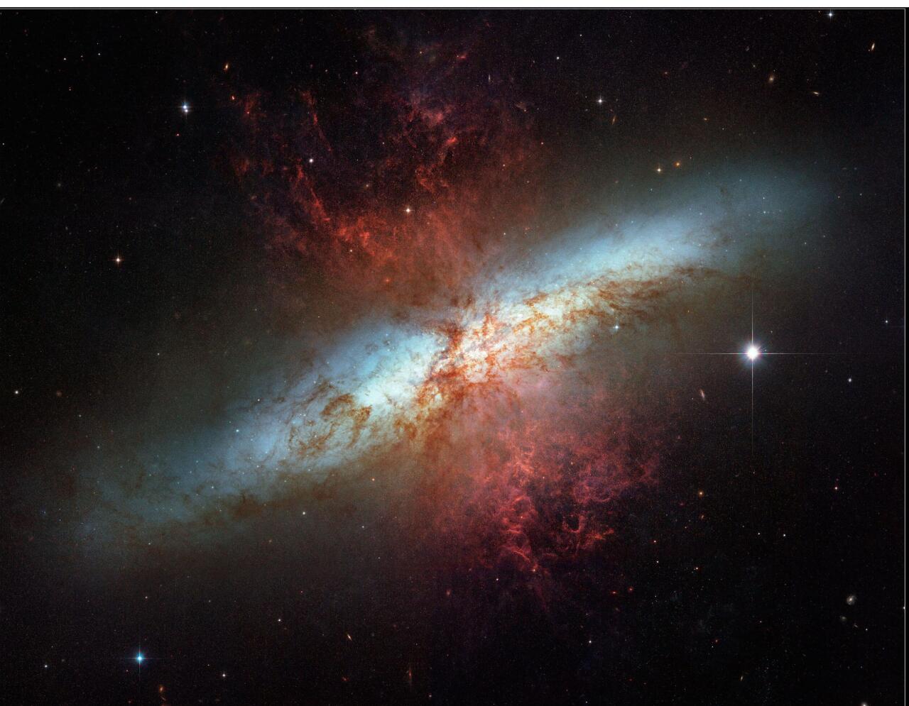 M82 galaxia irregularraren irudi ikusgaia kolore zuri eta urdinetan. Kolore gorrietan, galaxian sortzen diren izar berrien haizeak eta supernobek jaurtikitako hondakinak, hidrogenoaren igorpen-lerroen bidez irudikatuta