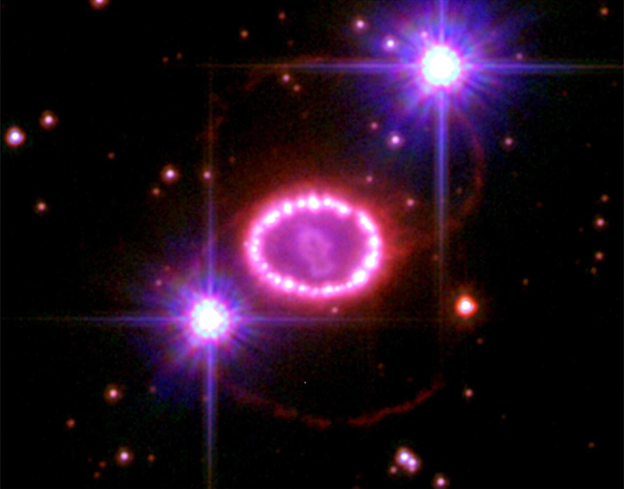 SN 1987A supernoba, <span style="font-style:italic">Hubble</span> teleskopioak hartutako irudian (2006ko abendua). Leherketa gertatu baino 20.000 urte lehenago izarrak sakabanatutako materialak osatzen du perlazko lepoko-itxurako egitura, eta argi-urte bateko diametroa du. Arrosa koloreko erdiguneko objektua lehertutako izarraren materiala da. Kanpoaldeko eraztun gorrien jatorriak misterioa izaten jarraitzen du. Irudian, Magallanesen hodeiko izar pare bat ere ikus daitezke